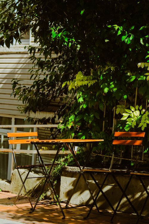Free Comfortable outdoor café setting with wooden chairs and table under lush greenery. Stock Photo