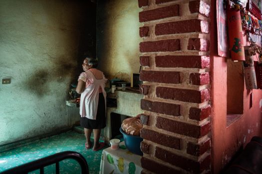Senior woman prepares meal in a rustic kitchen, showcasing traditional cooking style and atmosphere.