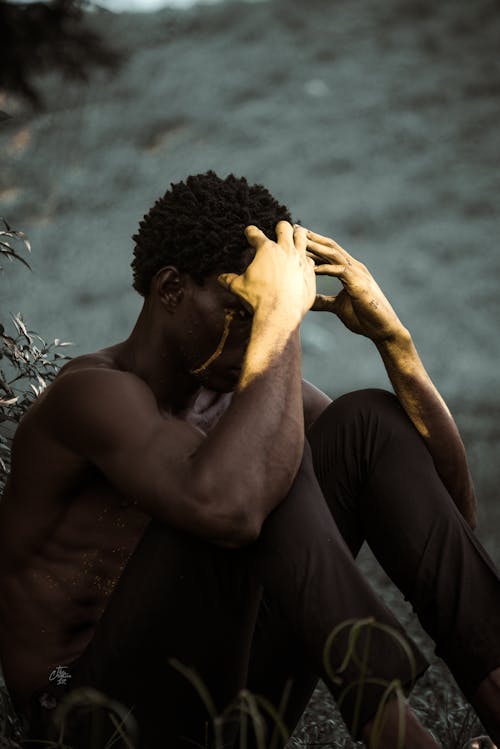 Shirtless Man Sitting on Ground in Nature