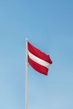 A bright Austrian flag waving on a flagpole against a blue sky in Vienna, Austria.