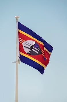 Eswatini flag waving on a flagpole against a clear blue sky, symbolizing national pride and identity.