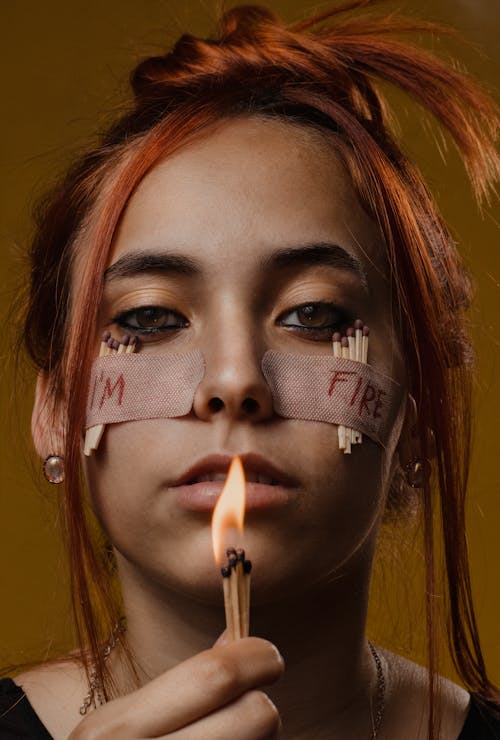 Free Woman with Band-aids and Matchsticks Taped to her Face Holding Burning Matchsticks Stock Photo
