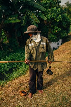 一名赤脚男子在郁郁葱葱的热带运河边钓鱼