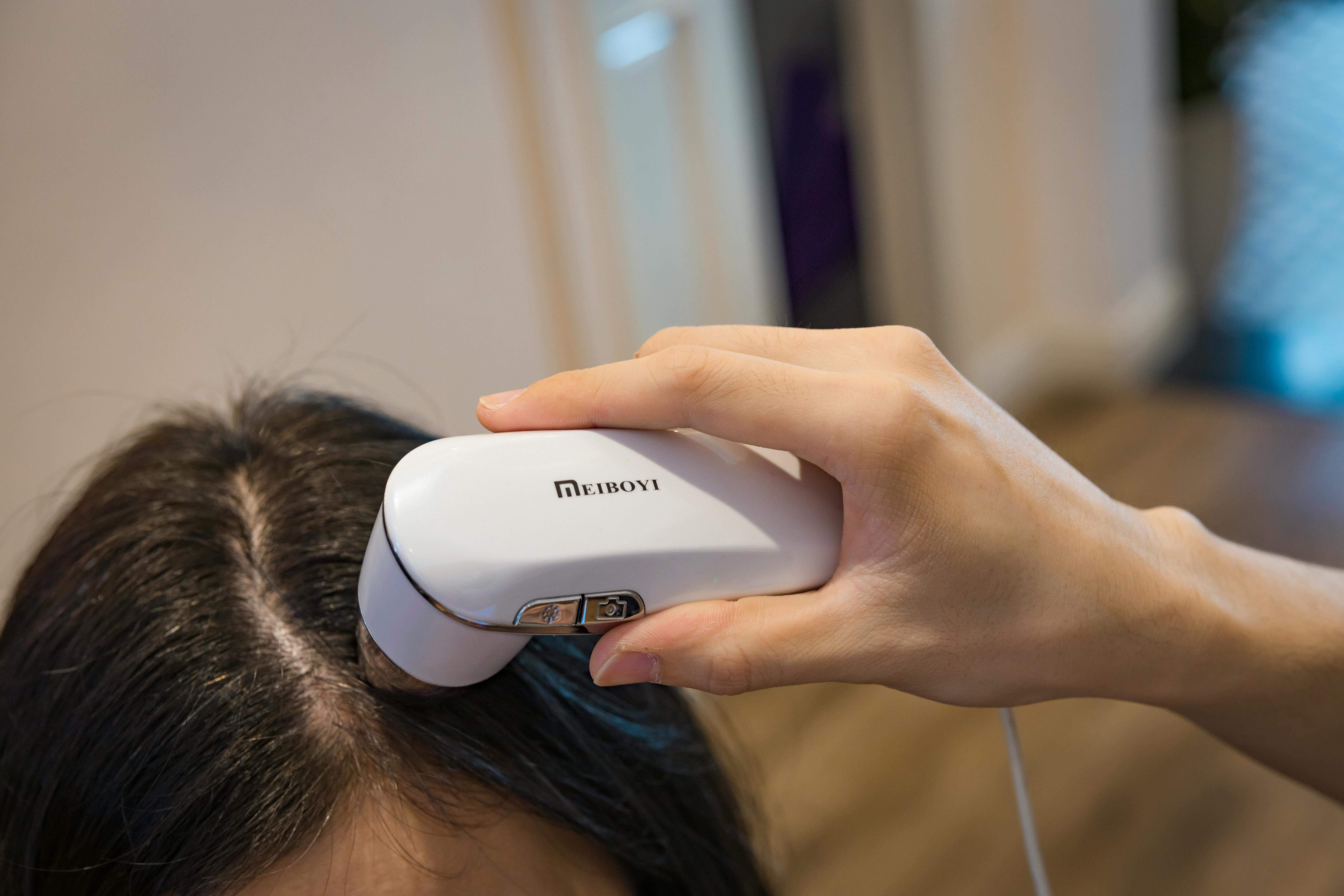 Close-up of a handheld device examining a person's scalp indoors.