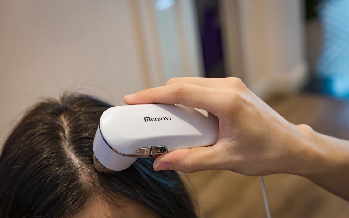 Handheld camera device examining the scalp along a woman's hair parting during a hair assessment
