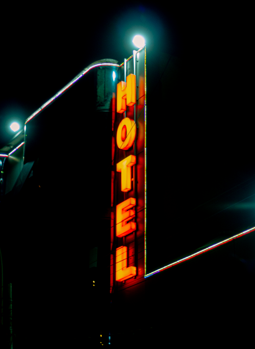 Free Illuminated neon hotel sign glows against the dark night sky, creating a striking visual scene. Stock Photo