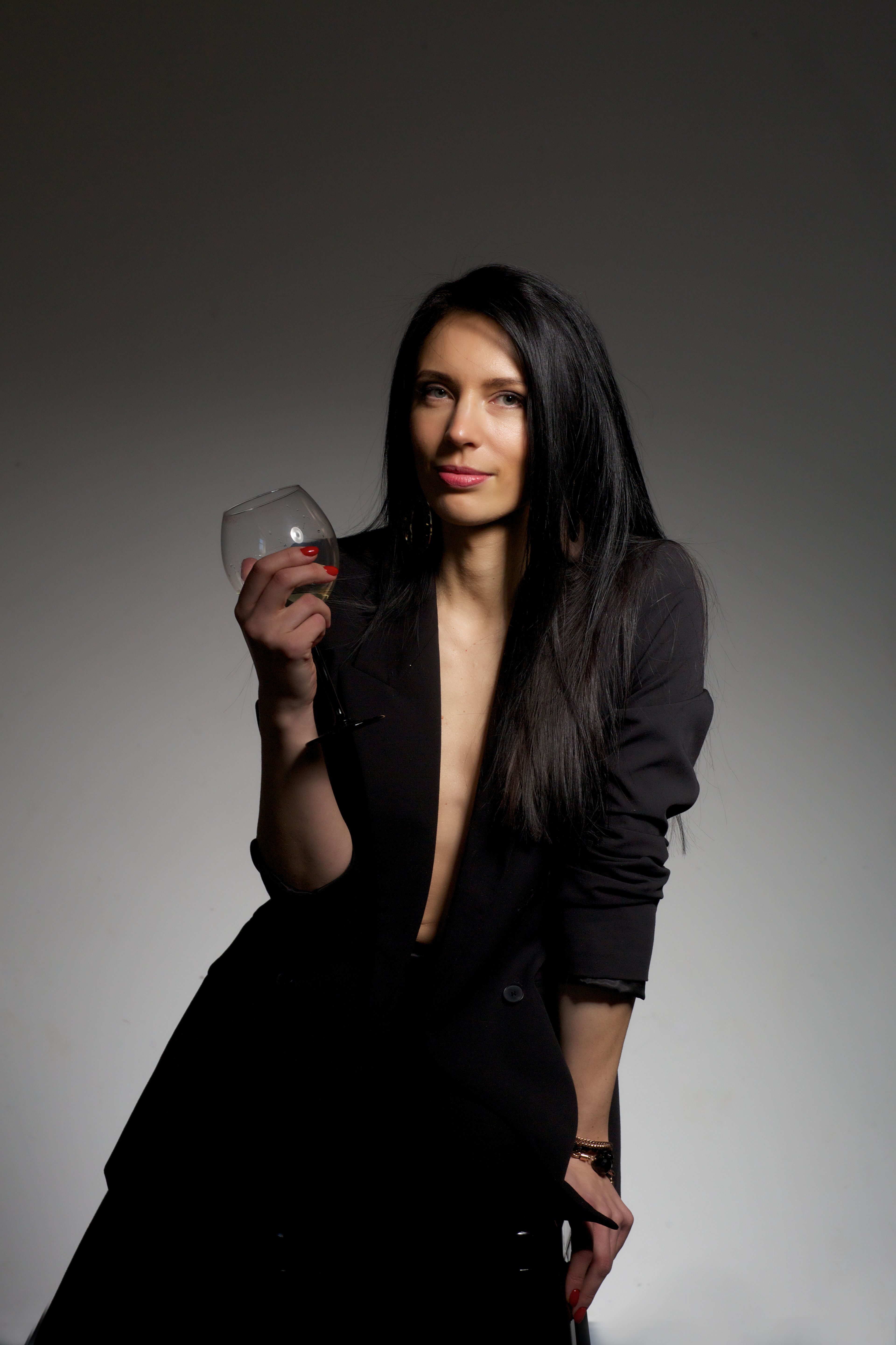 Portrait of a stylish woman posing with a wine glass in a studio setting.