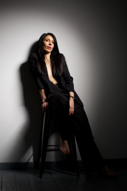 Free Portrait of a woman sitting in a dramatic spotlight, wearing a black suit. Captivating and artistic. Stock Photo