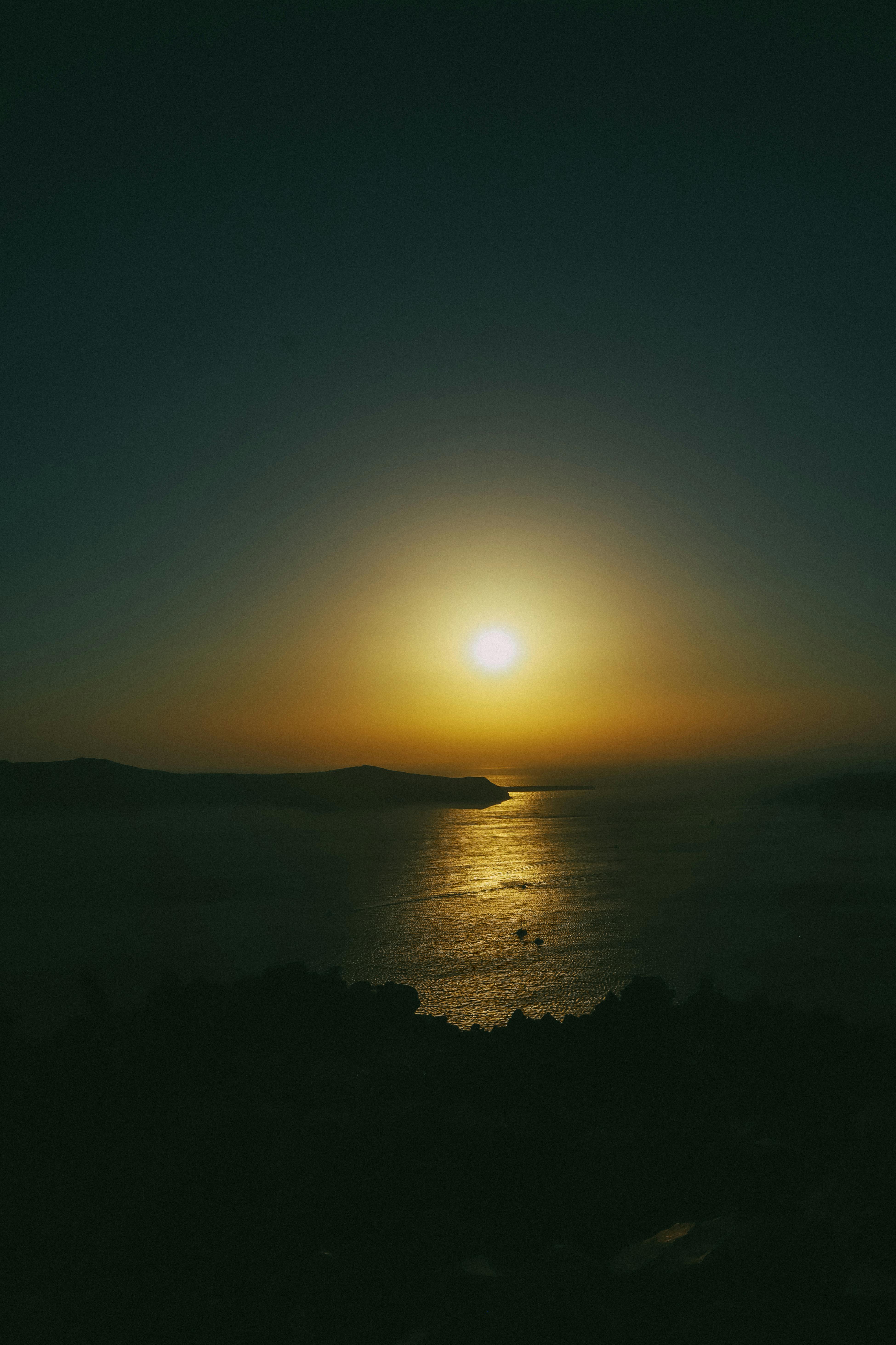 Free A tranquil sunset over the ocean, casting warm hues across the sky and water. Stock Photo