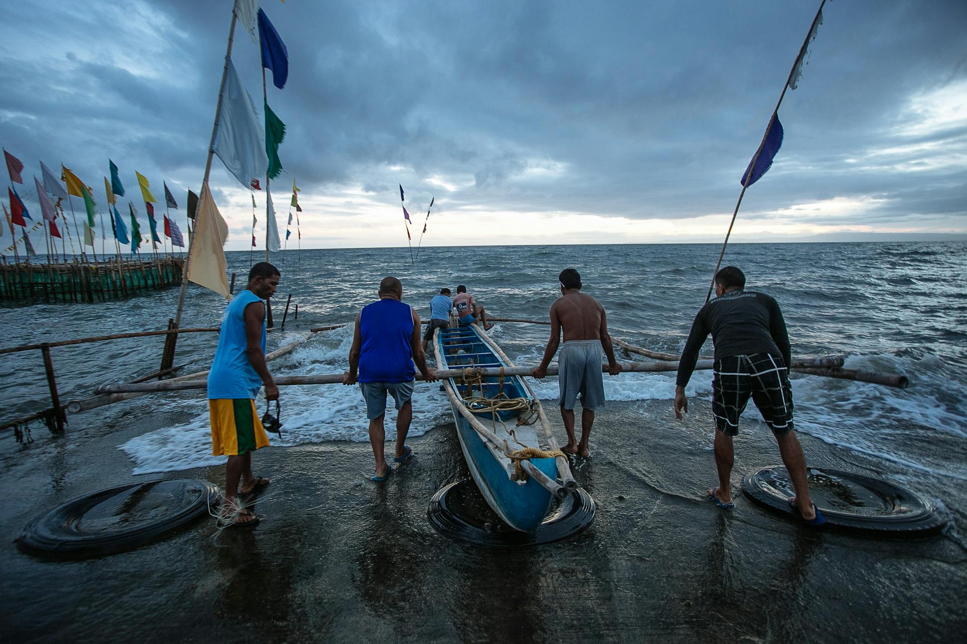 Group of fishermen launching a boat at Dumaguete seashore under a cloudy sky.