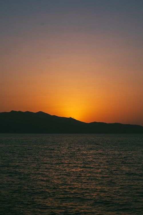 Free A breathtaking ocean view at sunset with silhouetted hills against a warm sky. Stock Photo
