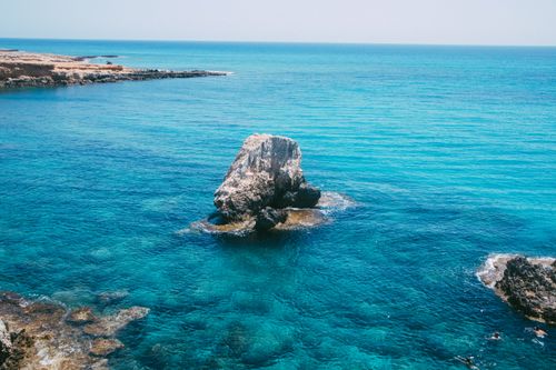 Free A serene coastal scene featuring clear blue waters and a solitary rock formation under a sunny sky. Stock Photo