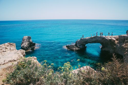 Free Tourists enjoy the scenic beauty and clear waters at a natural coastal arch. Perfect summer travel spot. Stock Photo