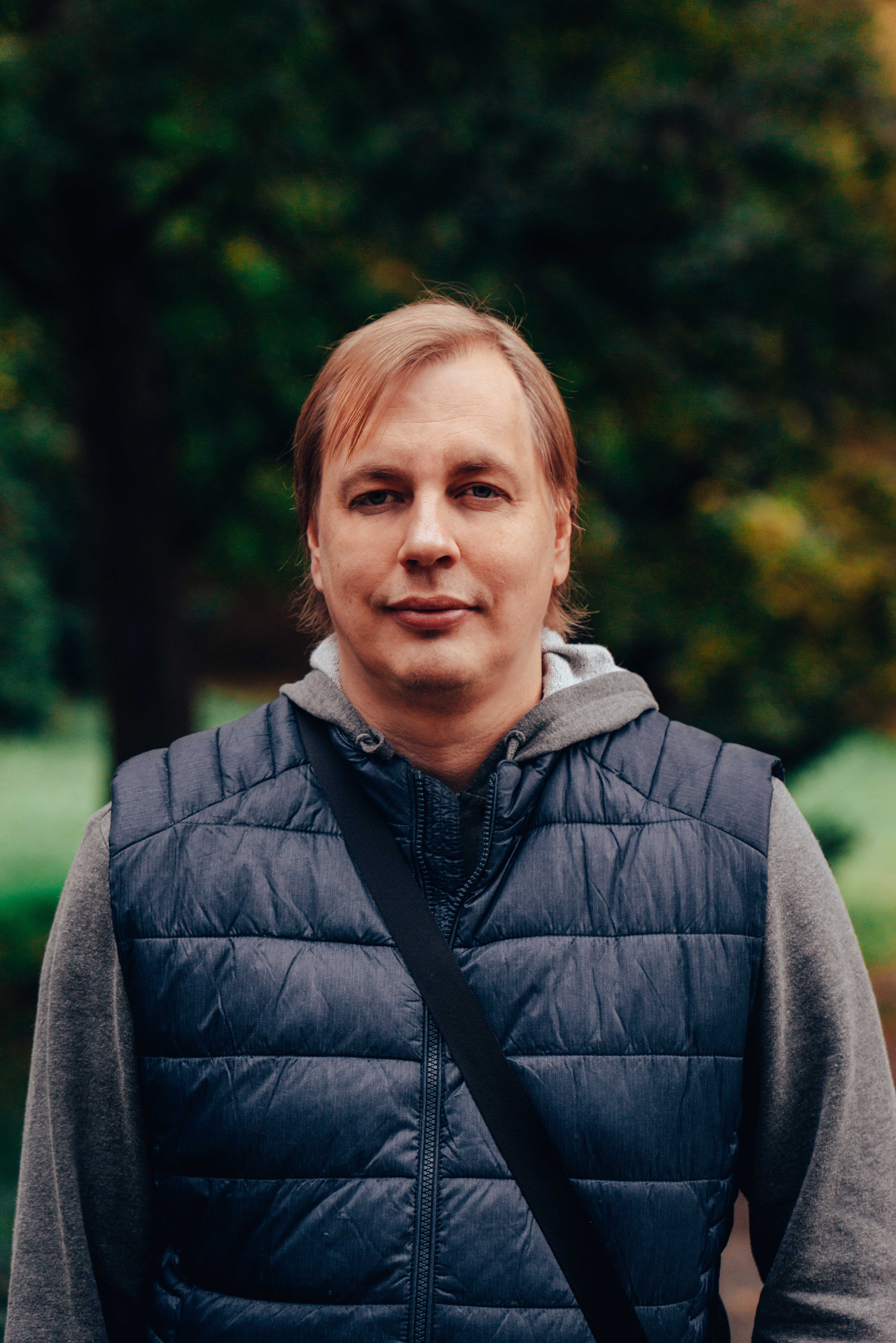 Portrait of a man in a blue puffer jacket outdoors with green background.