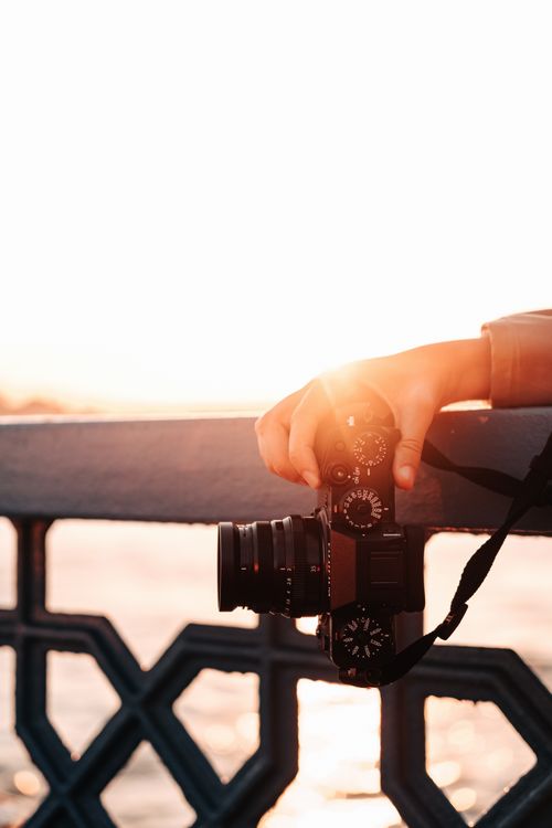 Free A hand holds a camera against a geometric railing at sunset, capturing the serene evening glow. Stock Photo