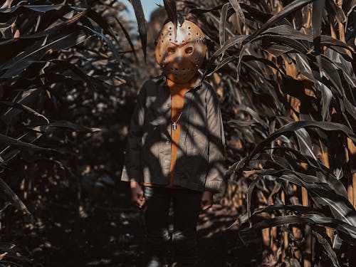 Man in Brown Jacket and Black Pants Wearing Mask Standing Between Plants