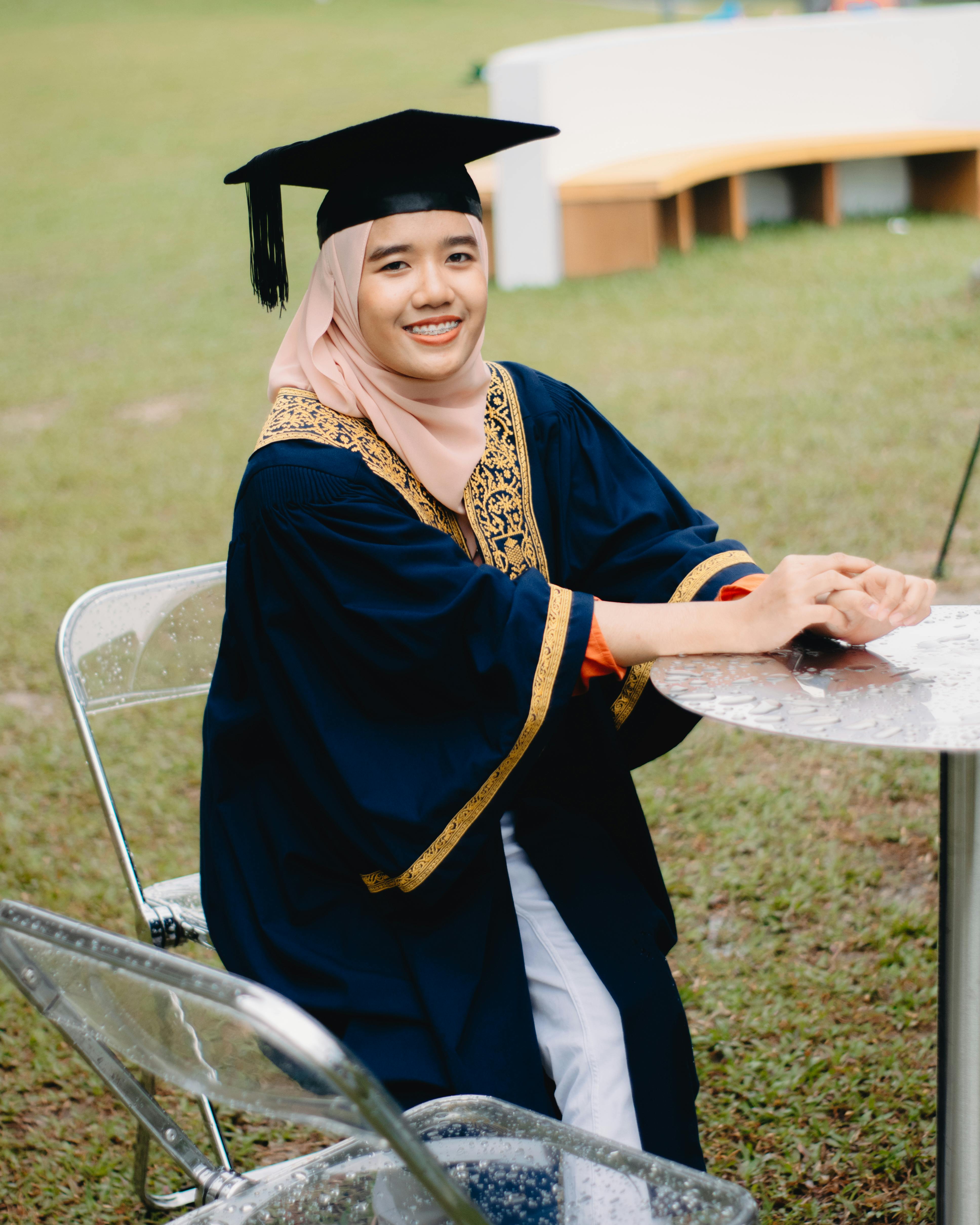 young woman in black graduation gown wearing beige hijab