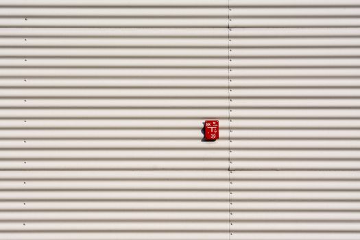 A minimalist white corrugated metal wall featuring a small red sign in the center.
