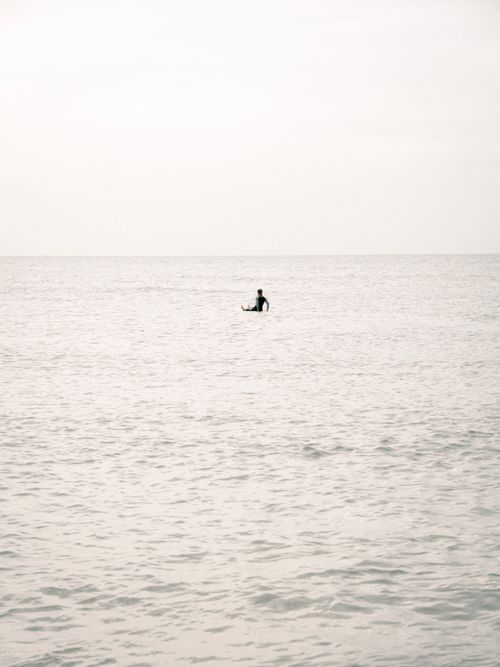 Free A person swims alone in a calm sea under an overcast sky, creating a serene and peaceful scene. Stock Photo