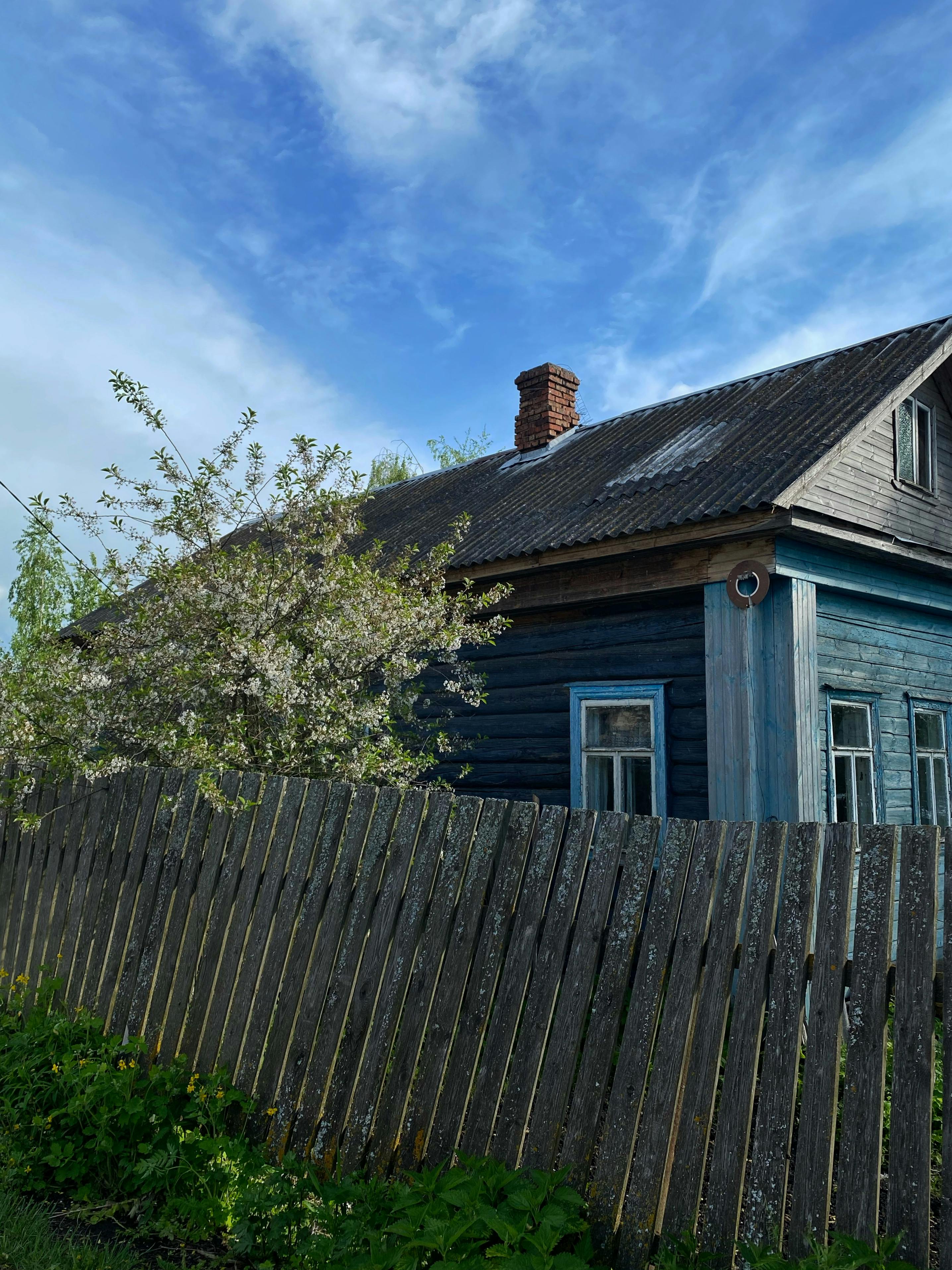 Quaint wooden house in Pereslavl-Zalessky, Russia, surrounded by a fence and greenery under a clear blue sky.