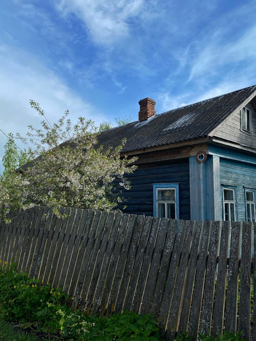 A Wooden House Near the Fence Under the Blue Sky and White Clouds