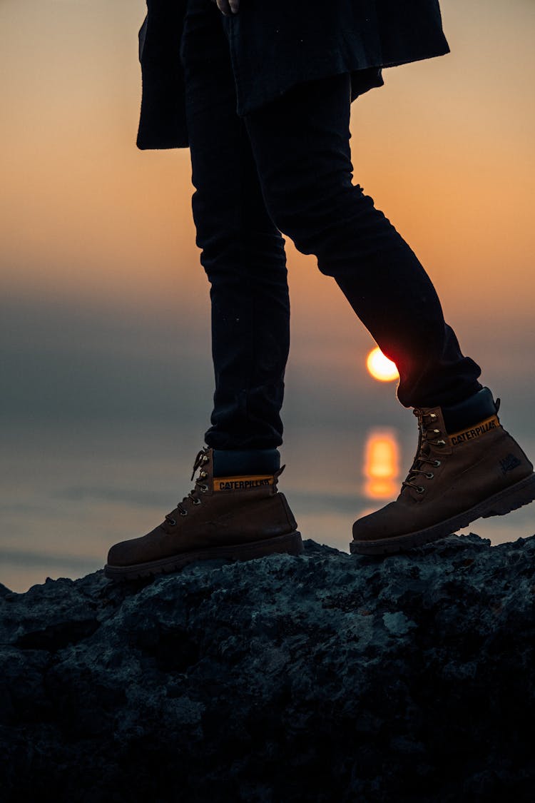 Man Standing On A Rock On A Seashore At Sunset 