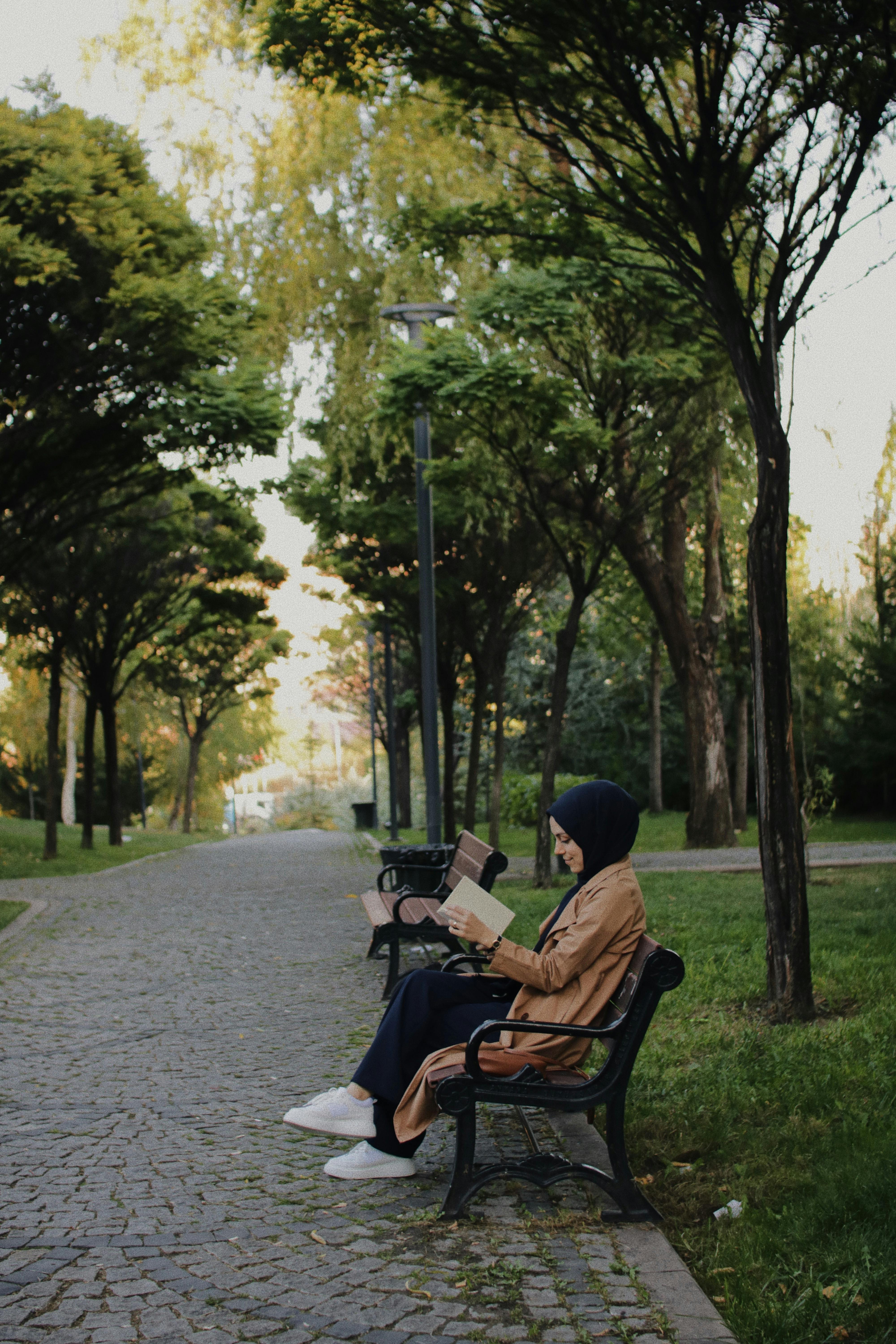 A woman enjoying a peaceful read on a park bench, captured during a serene fall afternoon.