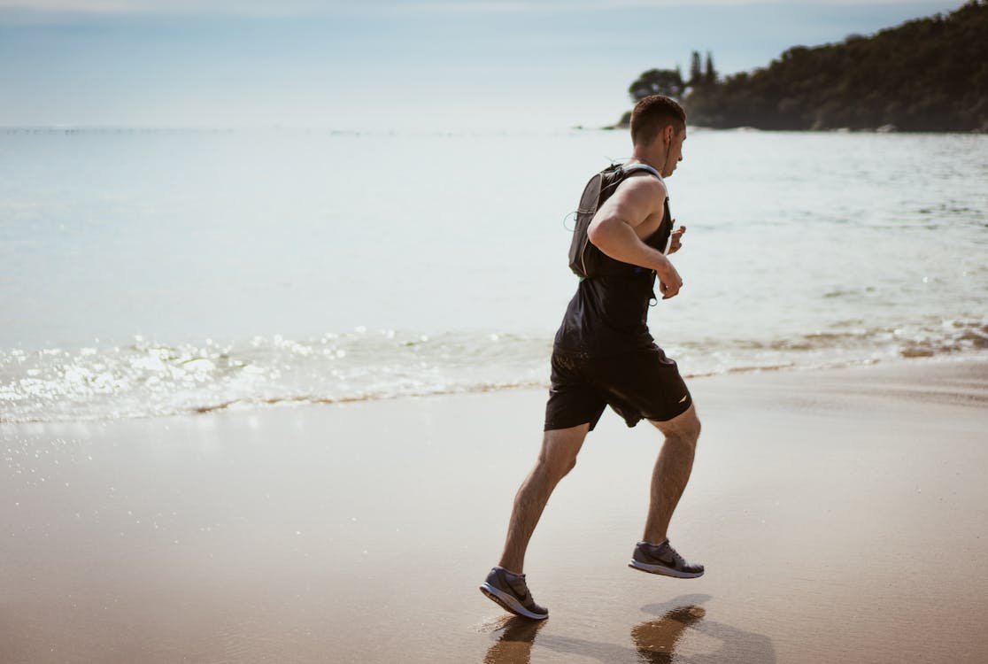 Free Man Wearing Black Tank Top and Running on Seashore Stock Photo