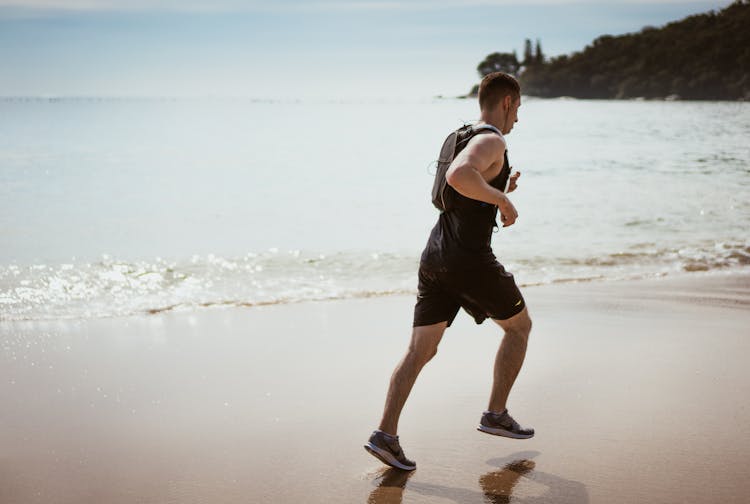 Man Wearing Black Tank Top And Running On Seashore