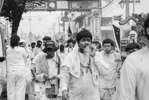 Free Men wearing white celebrate an outdoor festival in a bustling Thai street. Stock Photo