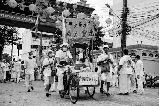 Black and white photo of a traditional street procession in Phuket, Thailand, featuring locals in cultural attire.