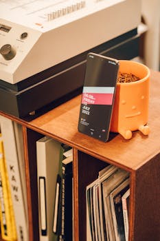 Smartphone leaning on a planter, displaying date on a wooden shelf with decor.