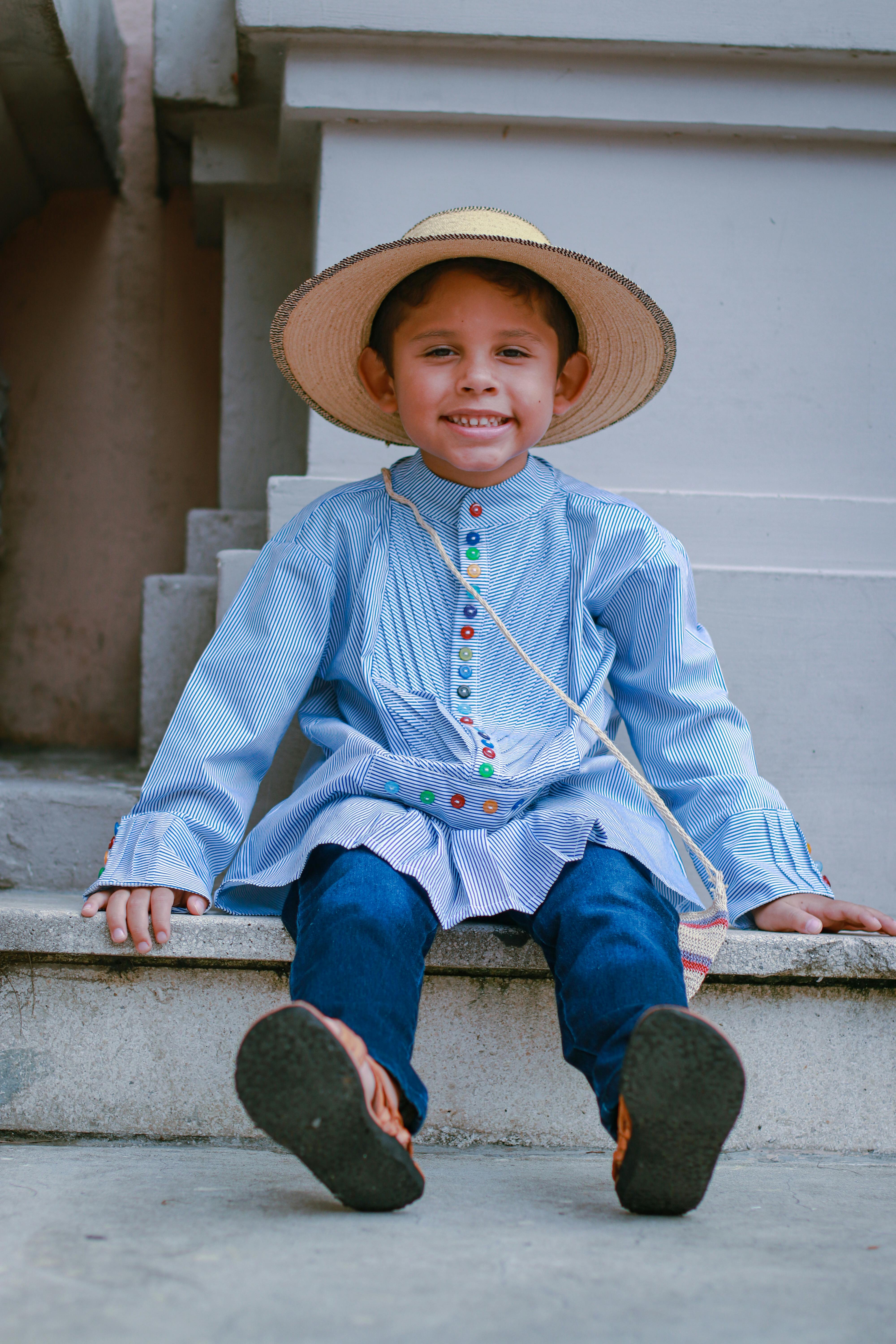 a boy in blue long sleeves smiling while sitting on the street