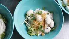Delicious traditional Thai noodle soup with herbs served in vibrant blue bowls, captured in Thailand.