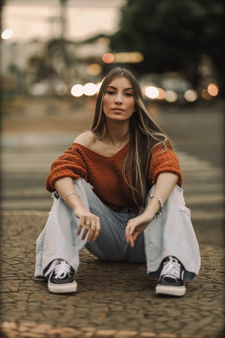 Woman In A Sweater And Jeans Sitting On The Pavement