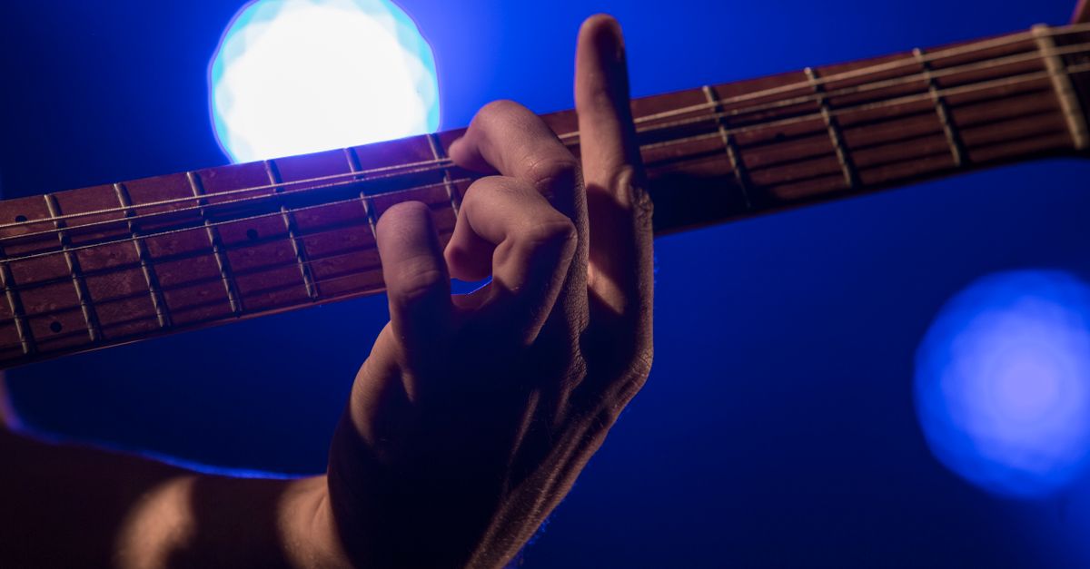 Close-up of musician's hands playing guitar with glowing screen in background
