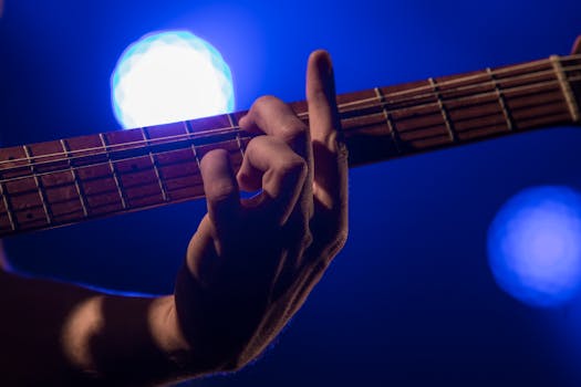 Close-up of a guitarist's hand playing guitar on a dimly lit stage, with blue lights in the background.