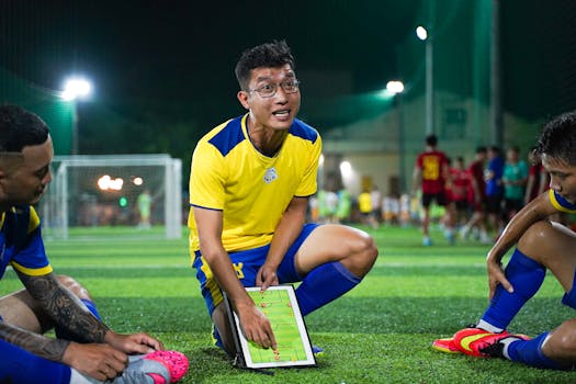 A soccer coach strategizing on a field with players during a night game session.