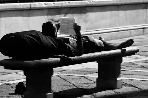 Free A man relaxes by reading a book on a bench in a Turin street scene. Stock Photo