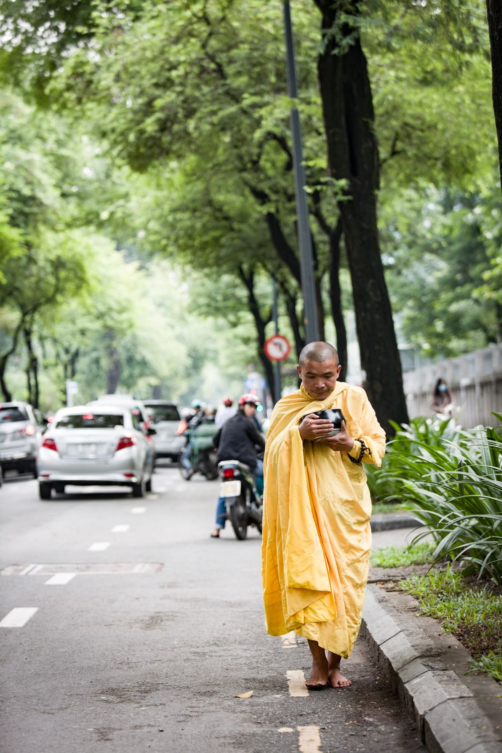 Monk holding an alms bowl while walking a city street