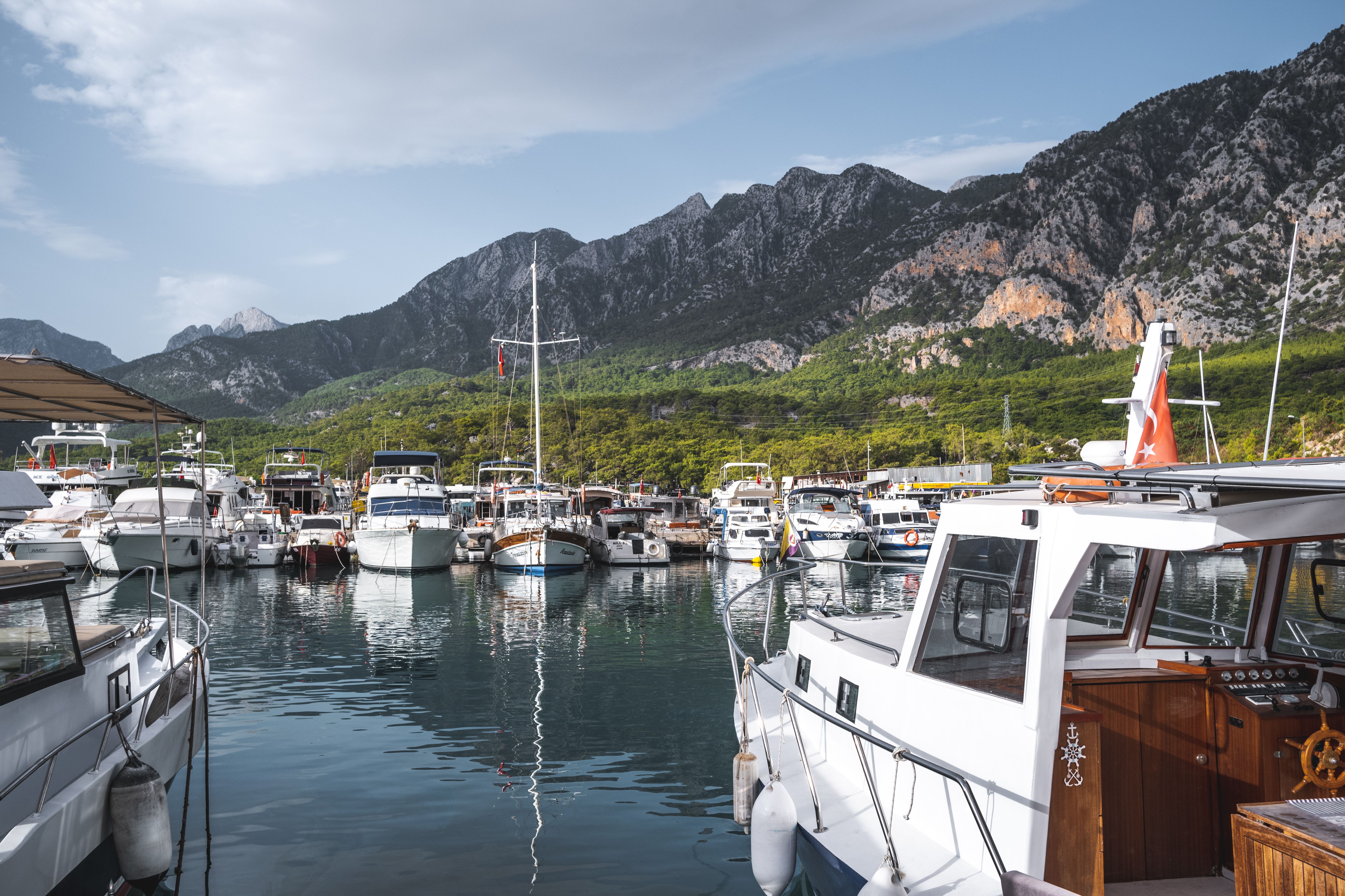 Scenic view of a marina with boats docked against a backdrop of majestic mountains under a clear blue sky.