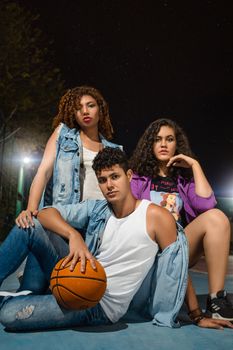 Youthful energy in urban fashion as three young adults pose with a basketball outdoors.