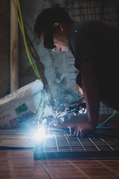 Free An adult male welder using protective eyewear, focused on welding metal with sparks flying. Stock Photo