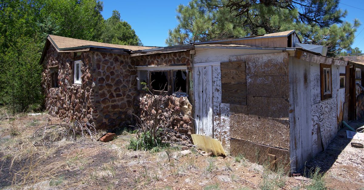 A neglected stone and wooden house surrounded by trees, reflecting rural decay.