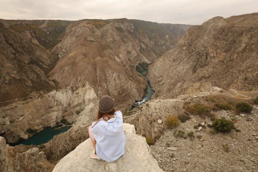Explore serenity with a woman sitting at the edge of a canyon, gazing at a stunning river gorge.