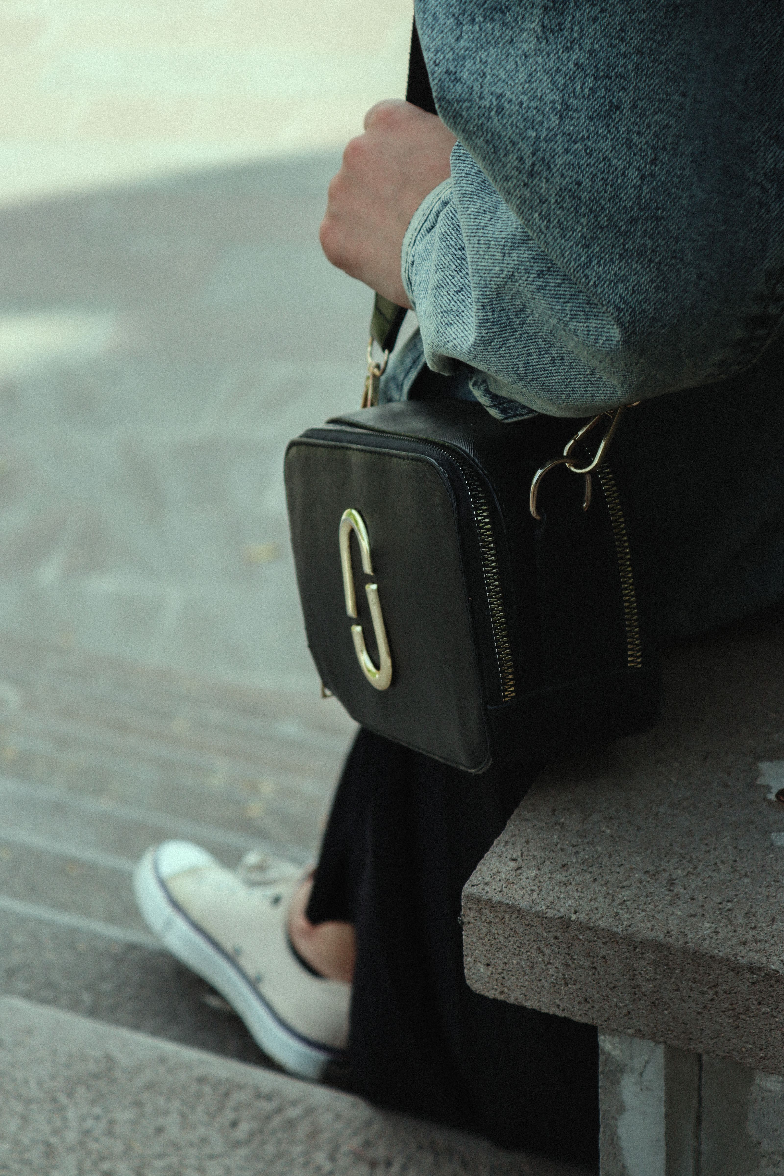 Close-up de uma elegante bolsa Marc Jacobs descansando em um banco de concreto, demonstrando um senso de moda moderno.