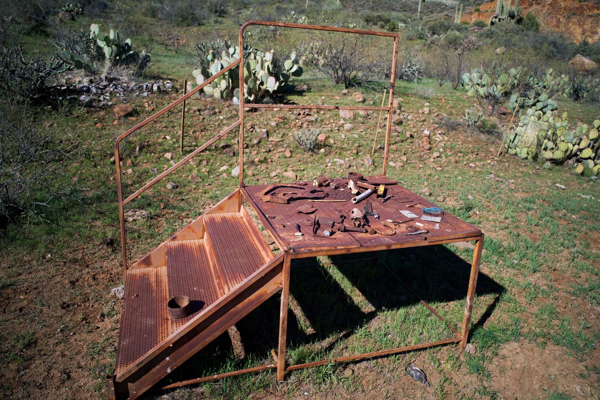 Rusty outdoor platform with assorted tools in a desert landscape, surrounded by cacti.