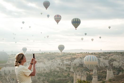Woman photographing hot air balloons in Cappadocia, Turkey at sunrise.
