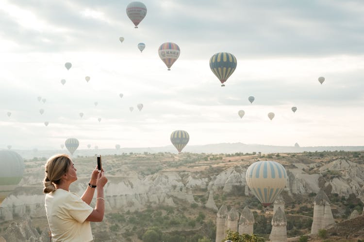 Woman Taking Photo Of Hot Air Balloons In Cappadocia