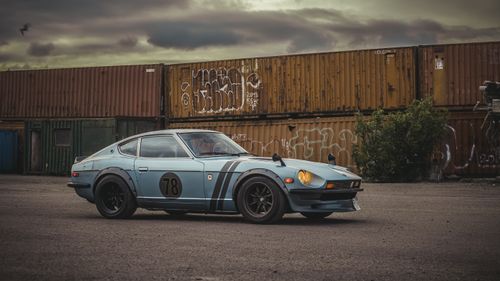 Free A classic Datsun sports car parked near cargo containers under a cloudy sky in Copenhagen. Stock Photo